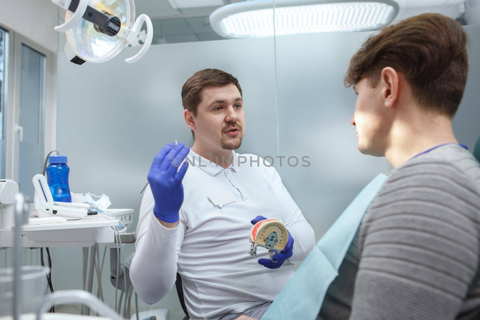 Young male dentist working at his clinic, talking to a patient
