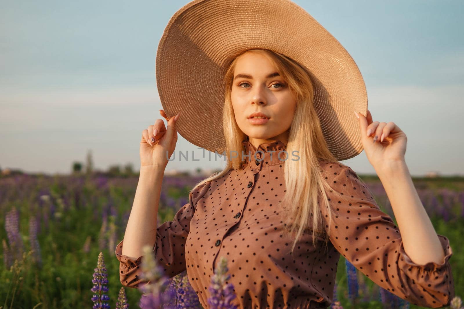 A beautiful woman in a straw hat walks in a field with purple flowers. A walk in nature in the lupin field.