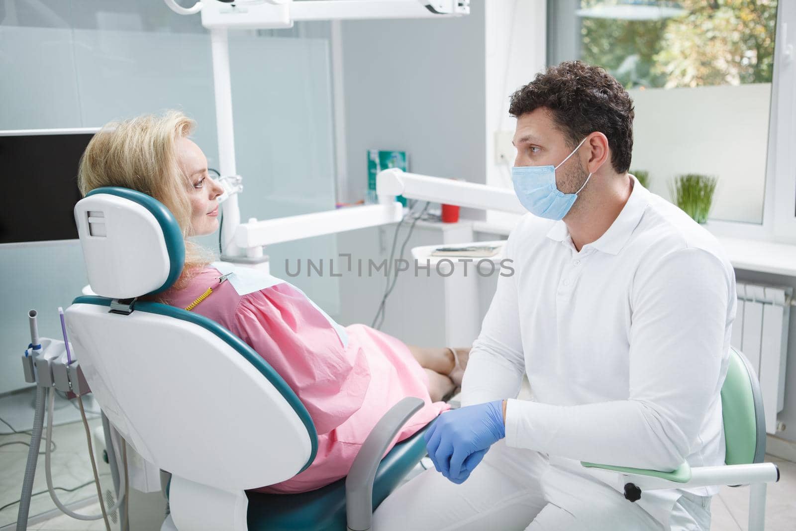 Male dentist wearing medical face mask, working with female patient