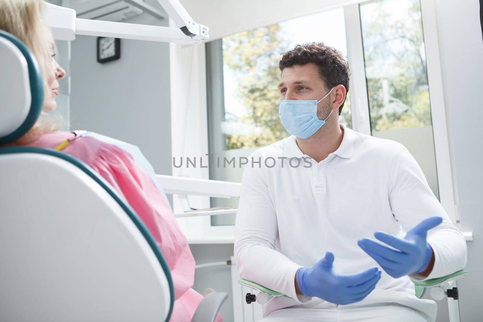 Professional dentist wearing medical face mask, talking to his patient
