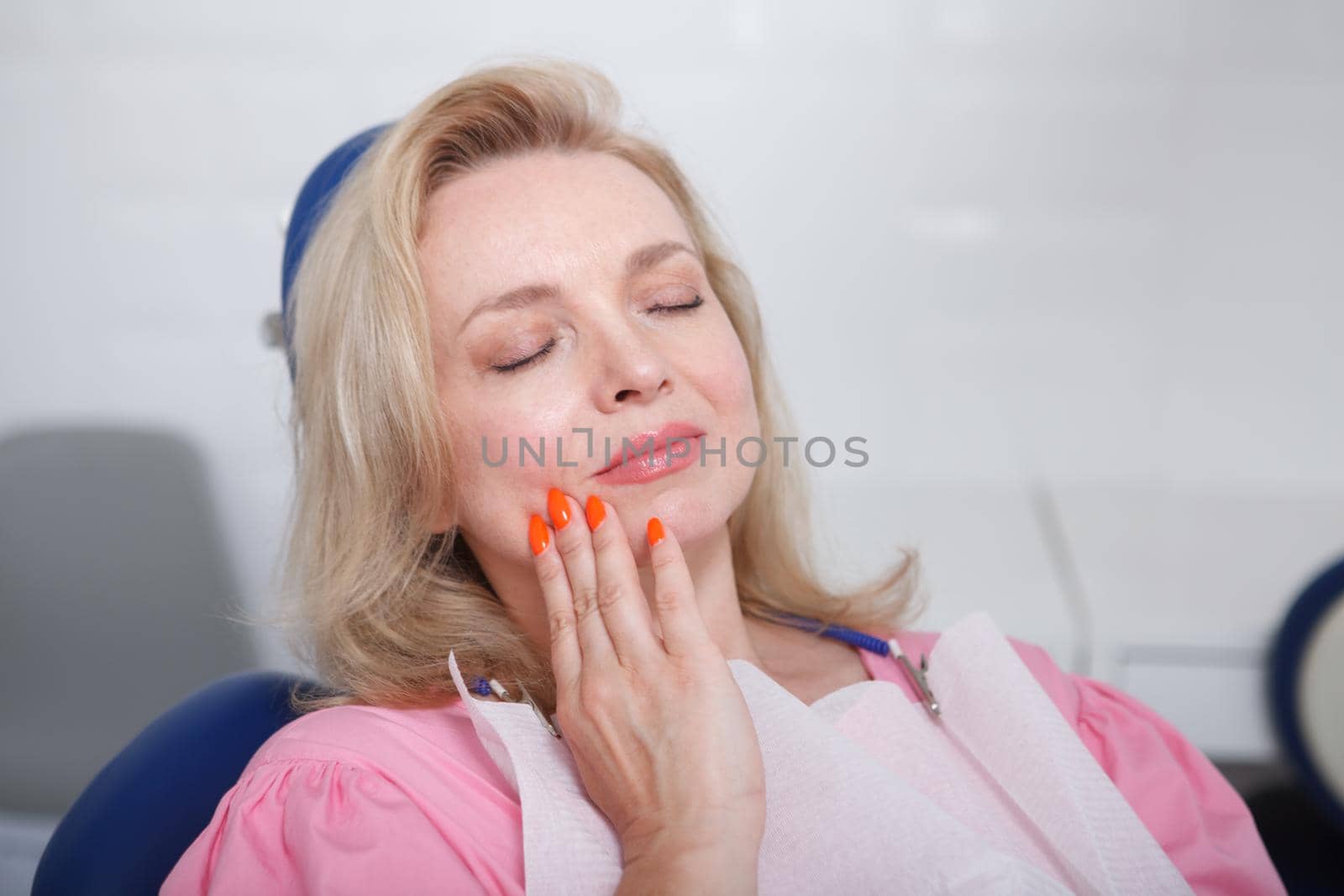 Middle aged woman having toothache, sitting in dental chair
