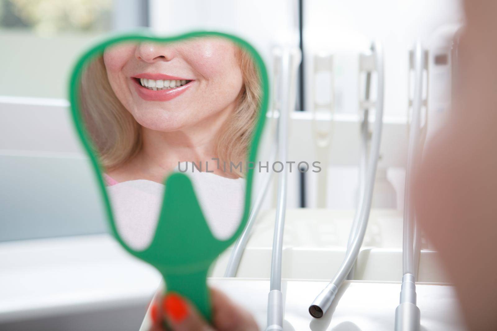 Close up of a mirror female patient is holding, looking at her teeth after dental treatment
