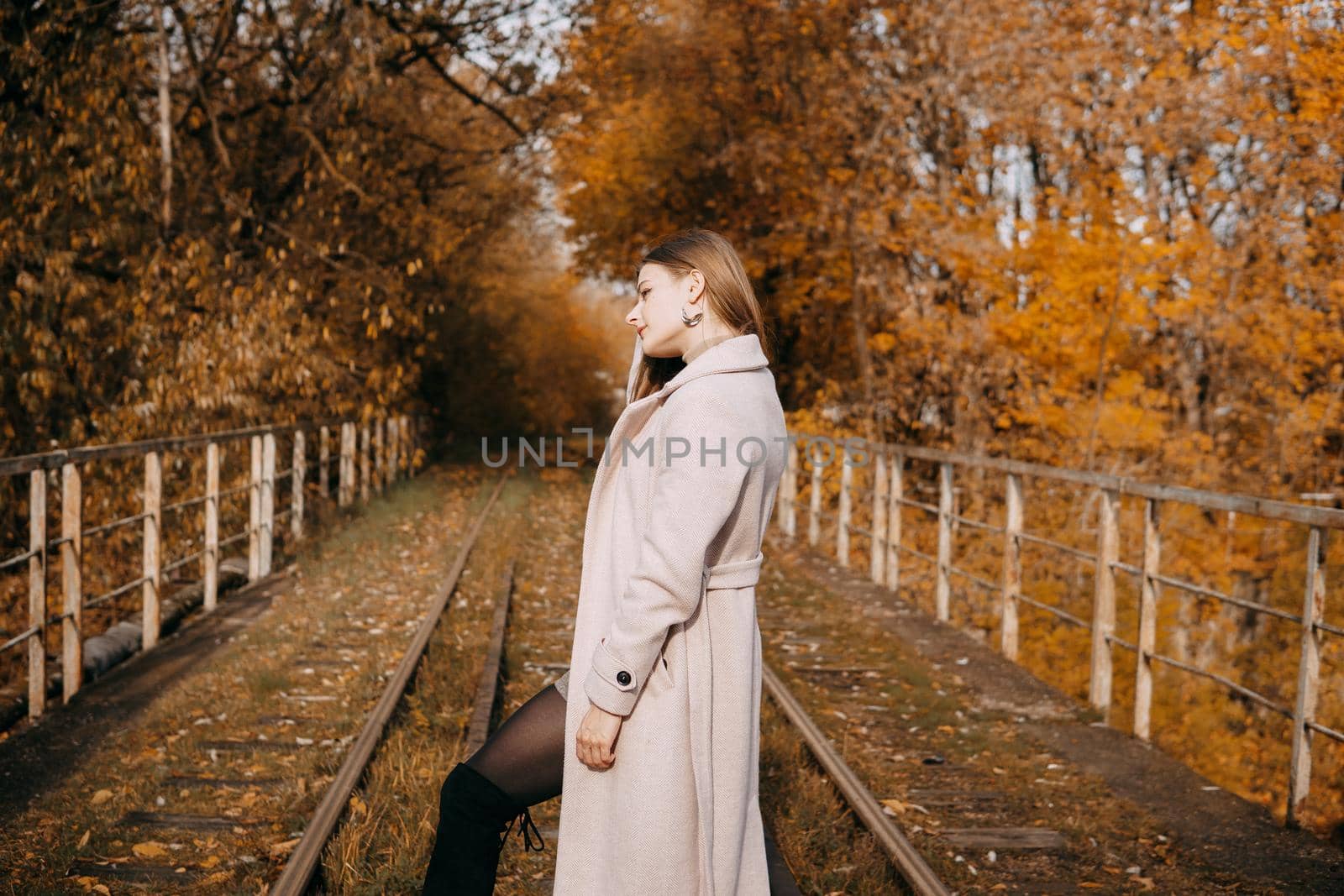 A beautiful long-haired woman walks through the autumn streets. Railway, autumn leaves, a woman in a light coat.