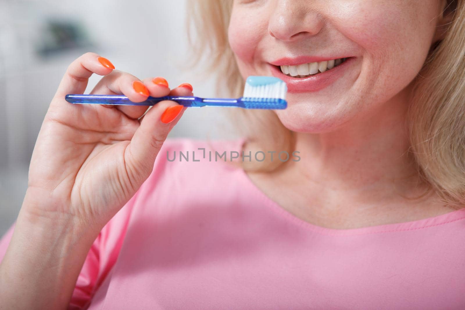 Cropped close up of a woman smiling, holding toothbrush with toothpaste