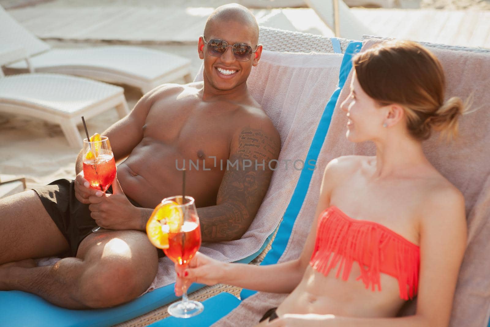 Handsome happy athletic man enjoying coktails with his lovely girlfriend at the beach. Young couple celebrating their summer vacation with drinks at the seaside