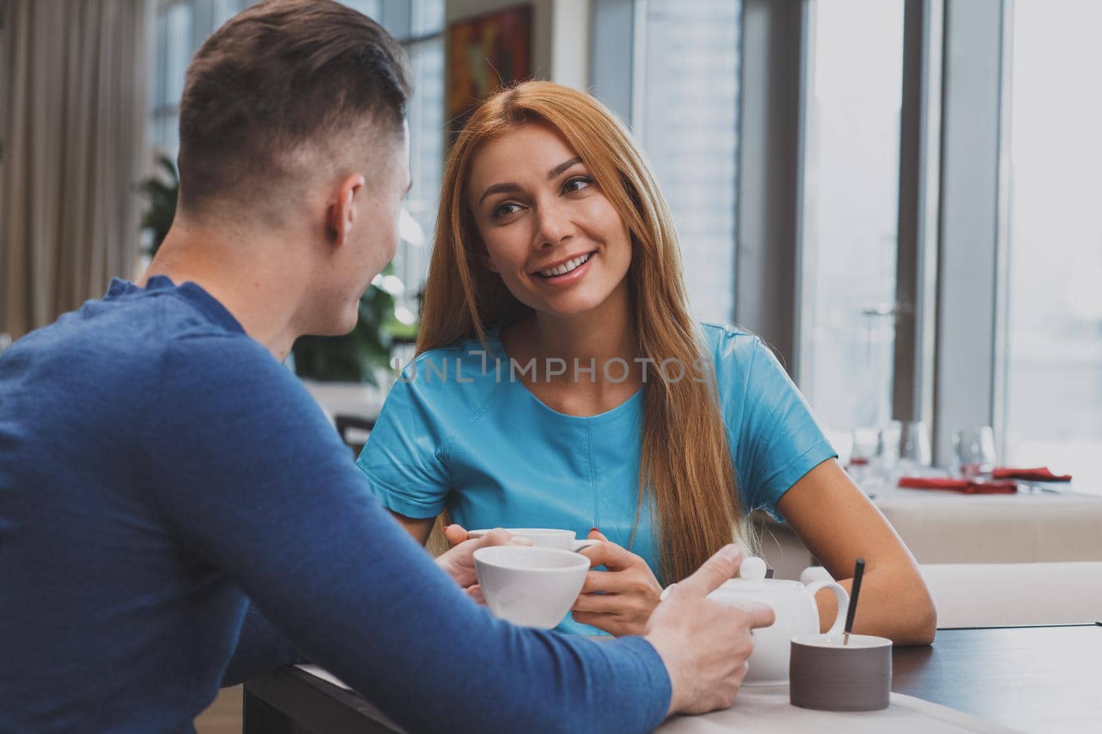 Gorgeous cheerful woman smiling, enjoying having coffee with her boyfriend at the local restaurant. Lovely couple having breakfast together at the cafe, celebrating anniversary