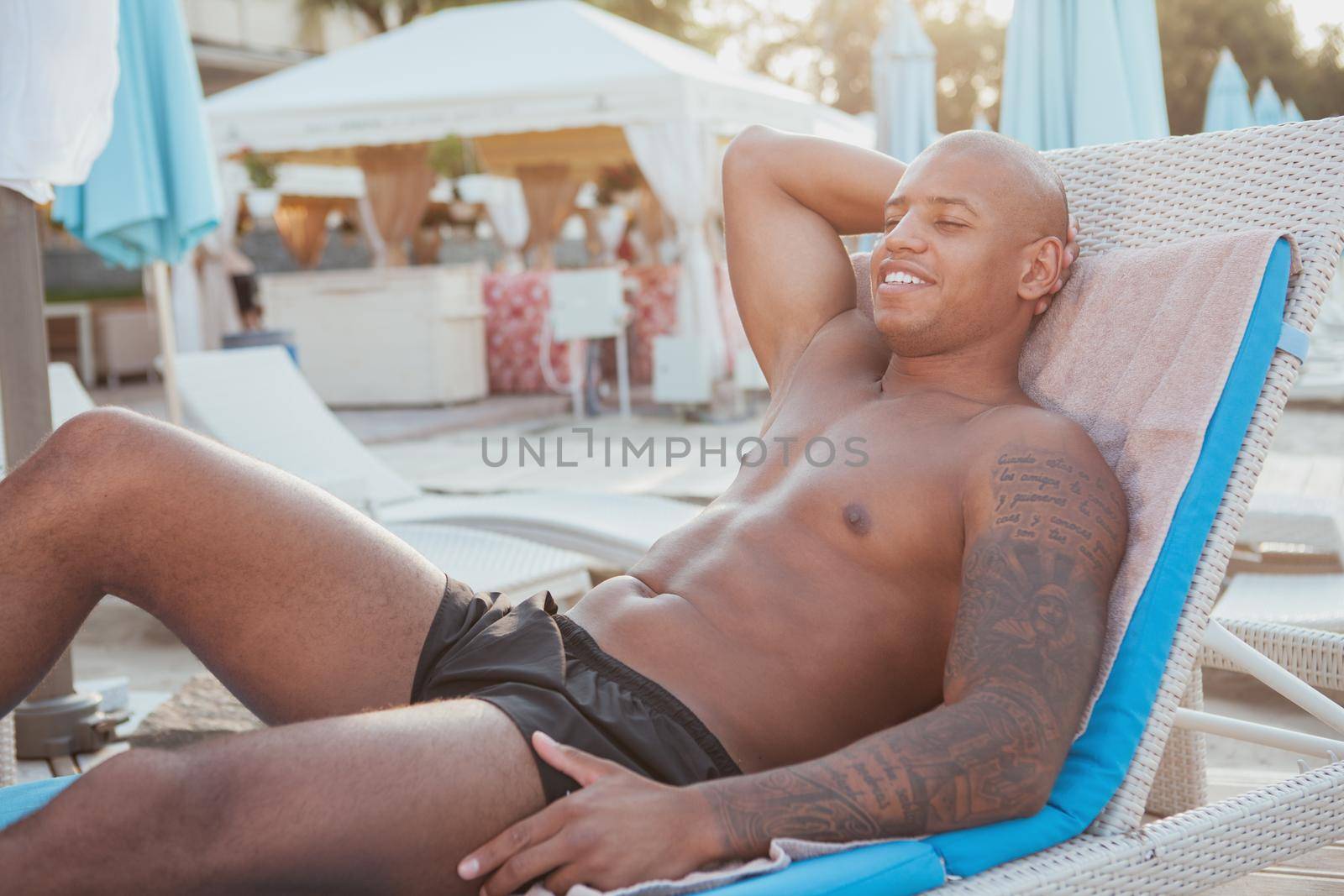 Handsome athletic African man sunbathing at the beach by MAD_Production