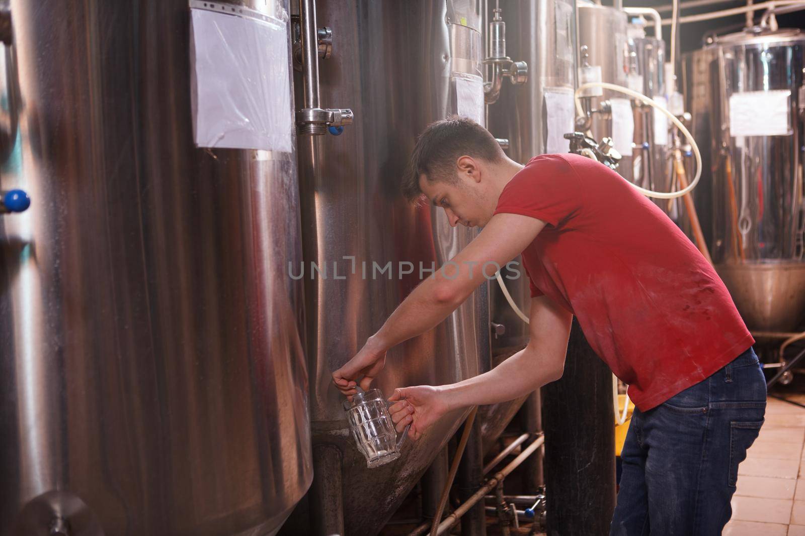 Brewery worker pouring fresh beer from metal tank into a glass