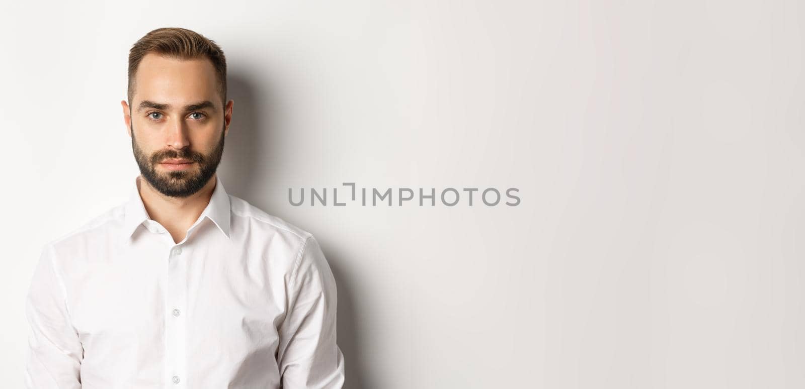 Close-up of serious businessman in white shirt looking at camera, standing confident.