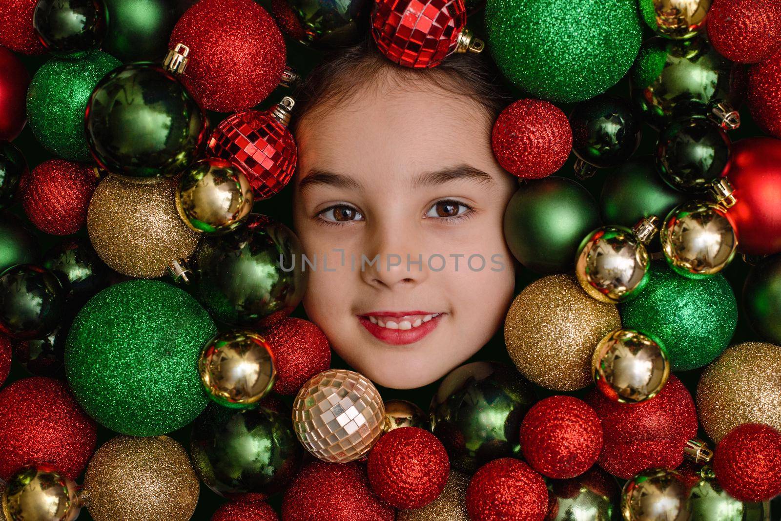 Cheerful portrait of a little girl in red, green and gold Christmas balls.