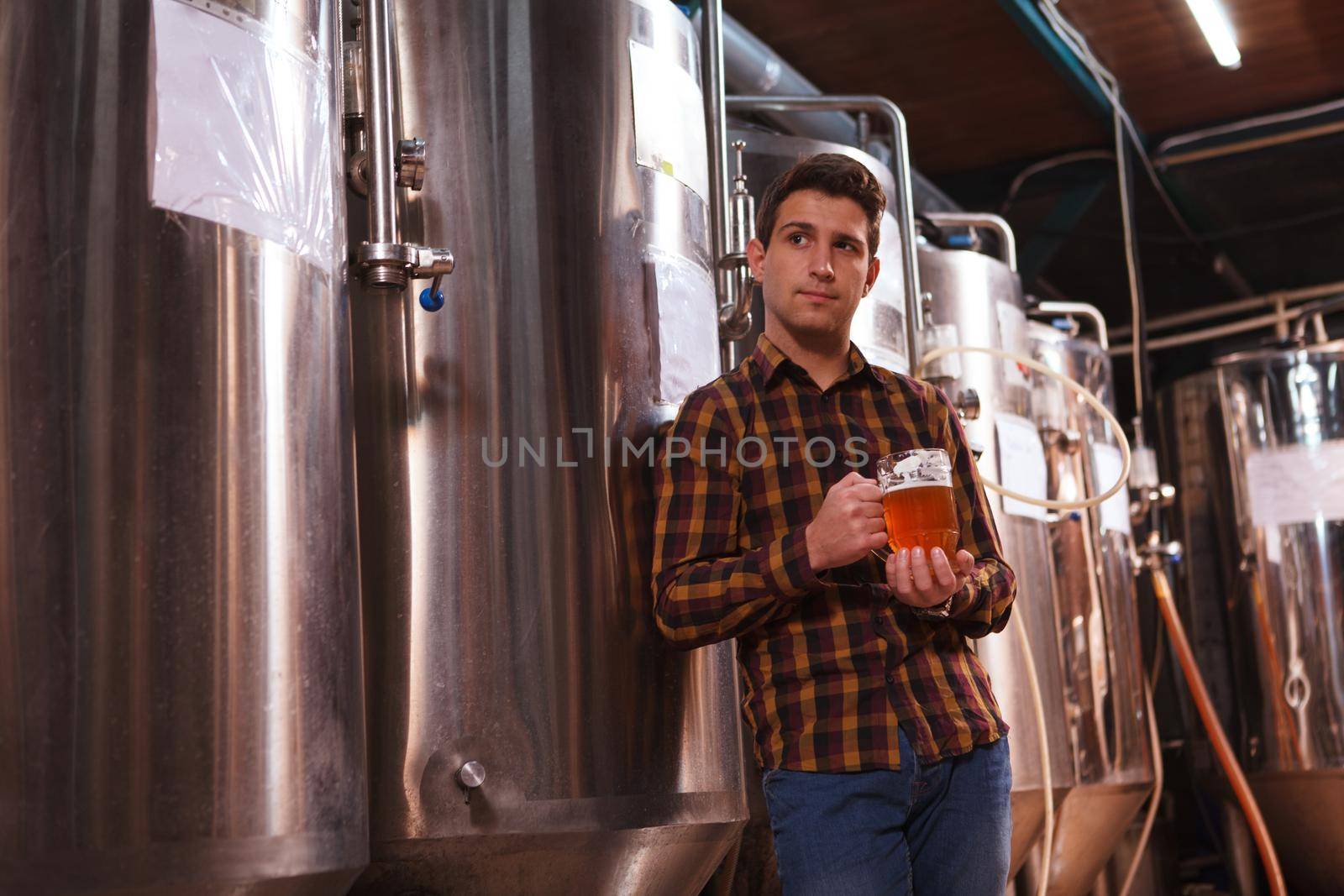Handsome male brewer resting at his brewery after working day, having glass of beer