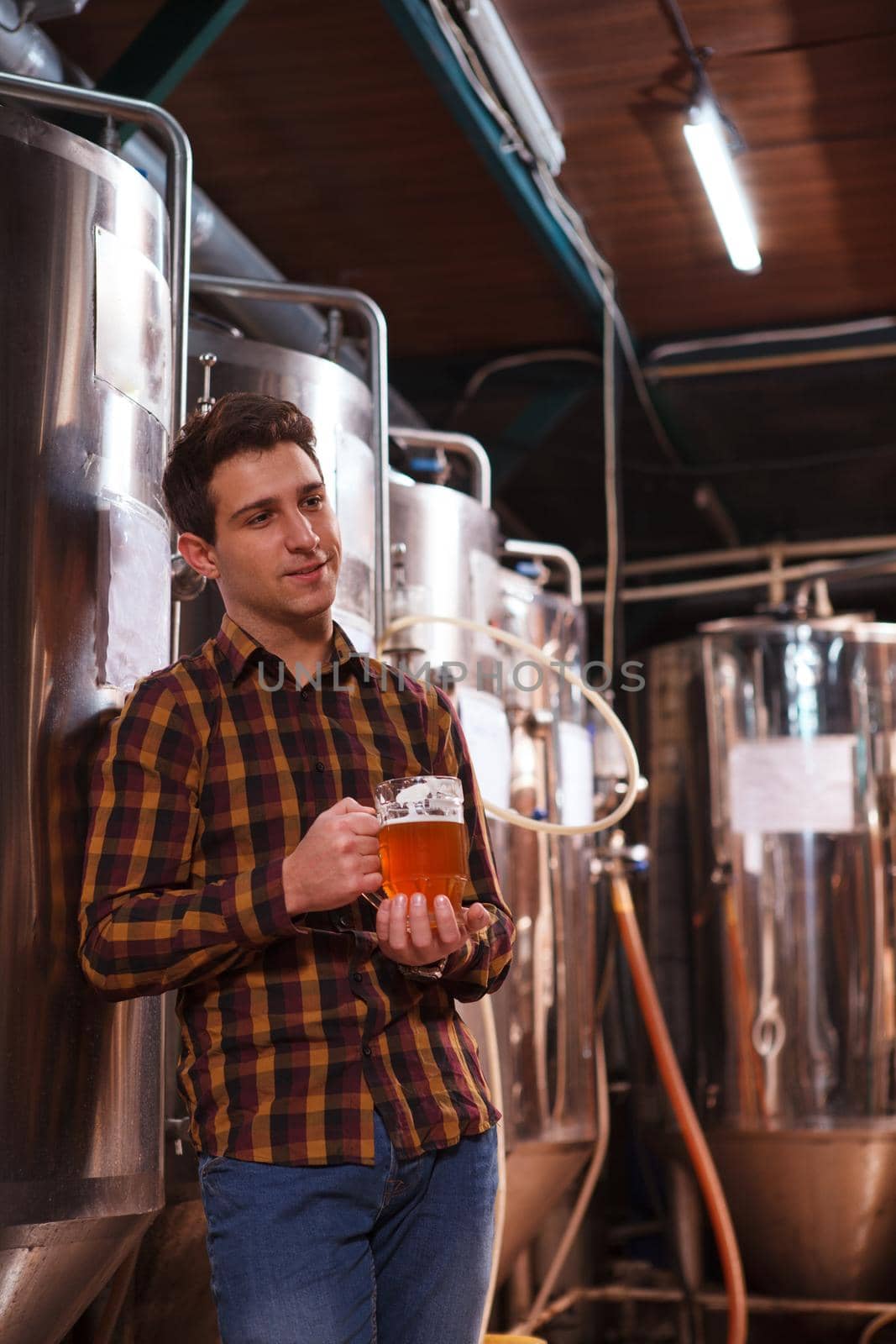 Vertical shot of a brewer relaxing after working at his microbrewery, having mug of beer