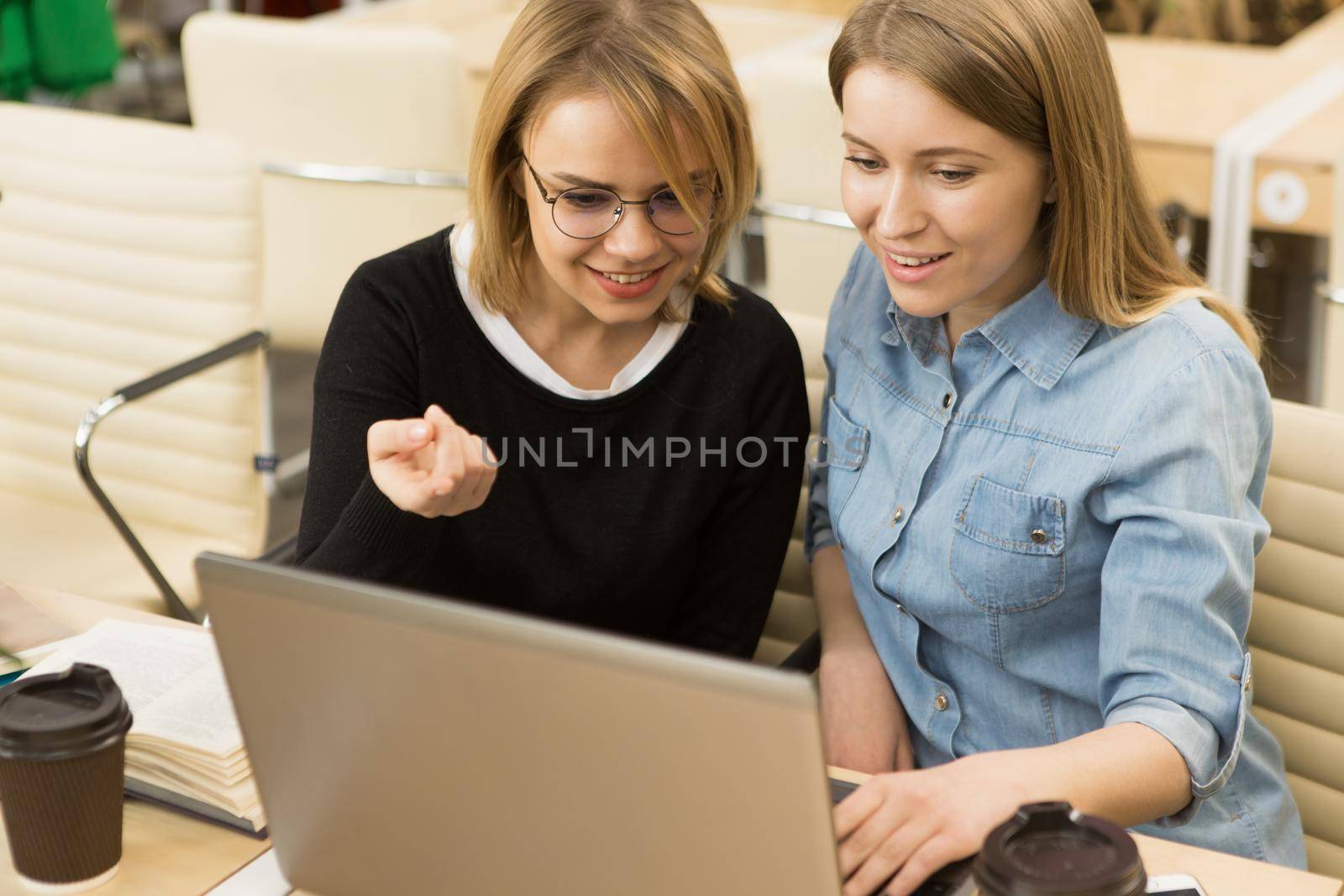 Two beautiful female coworkers working on a laptop together at the office communication teamwork technology browsing online internet wireless 3g 4g friendship friends gossip chatting talking studying