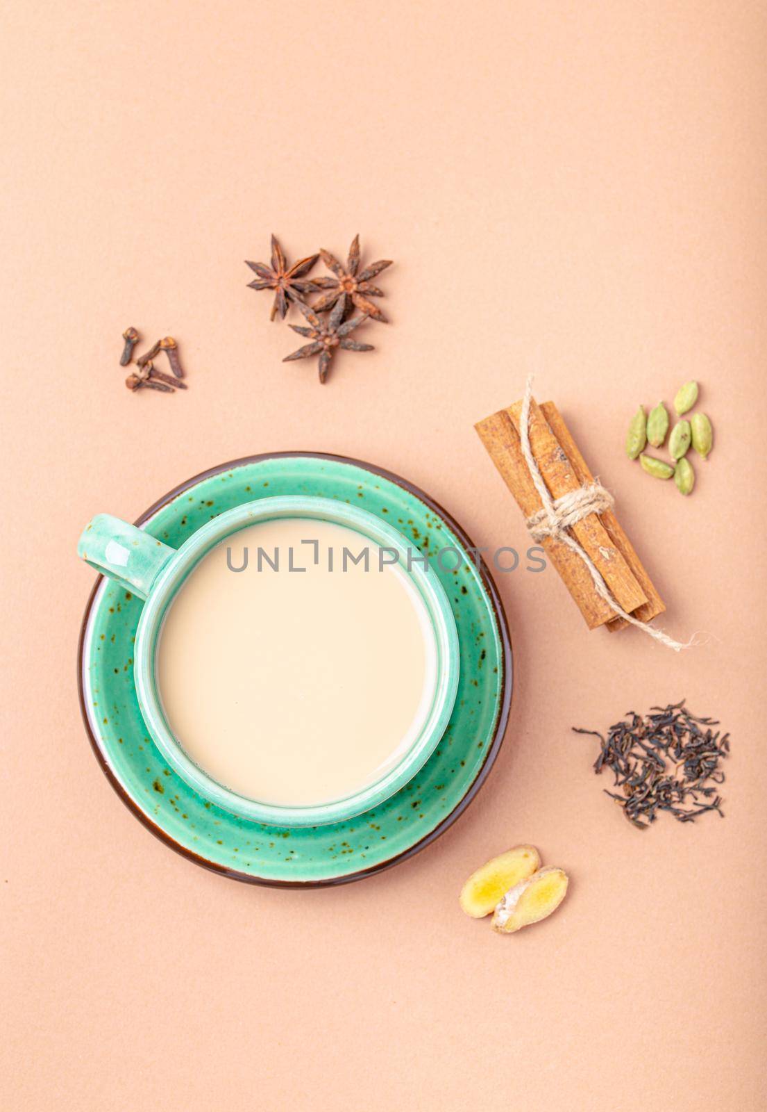 Healthy Indian beverage masala chai - tea hot drink with milk and spices in rustic green teacup with ingredients for making masala chai from above on simple beige minimal background