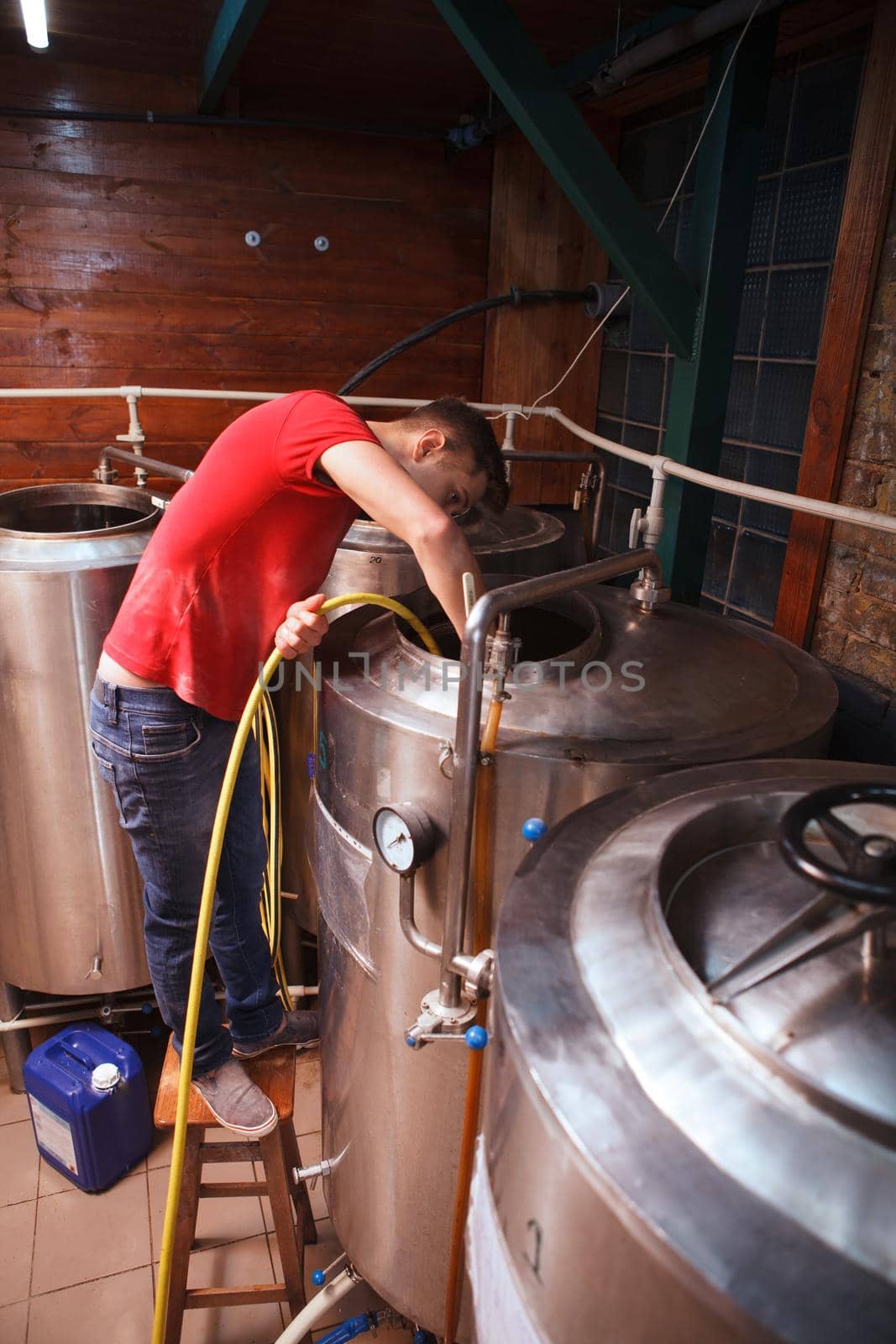 Vertical shot of a microbrewery technician using water hose, cleaning inside beer tank