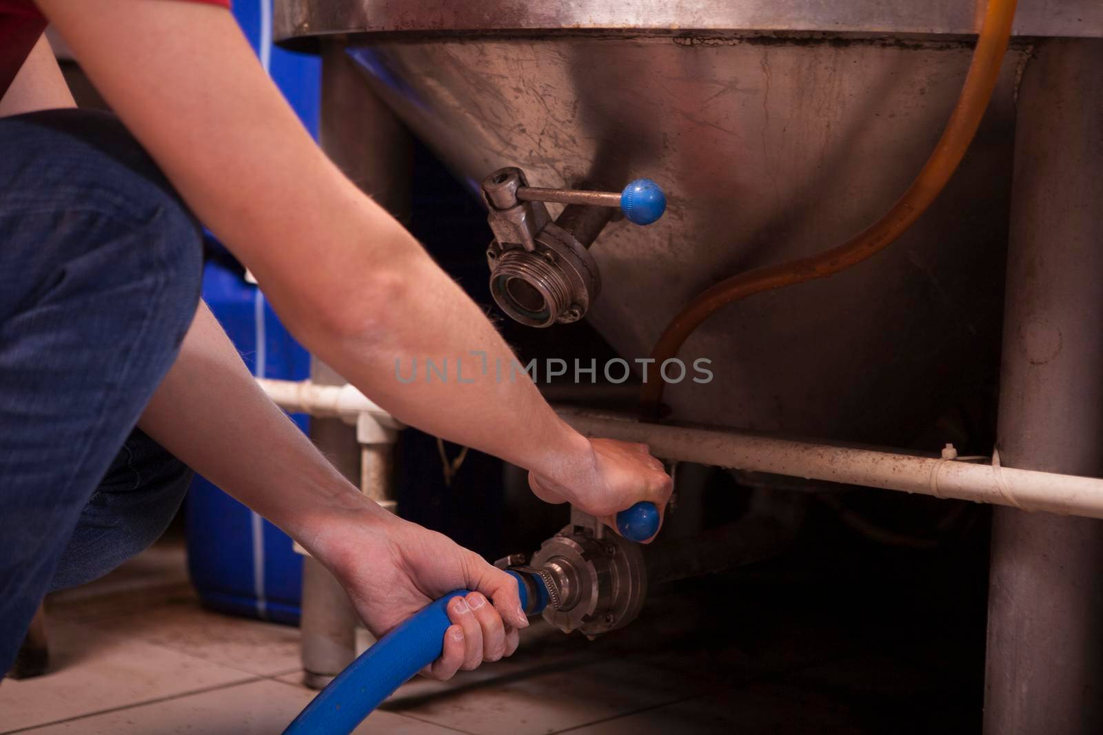 Unrecognizable man connecting a hose to a steel tank, working at manufacturing