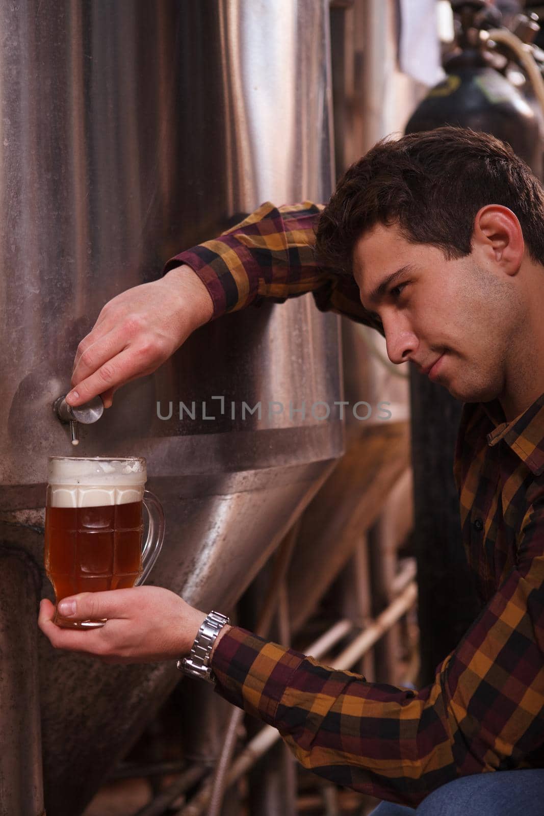 Vertical cropped shot of a professional brewer pouring freshly brewed beer from metal tank into a mug