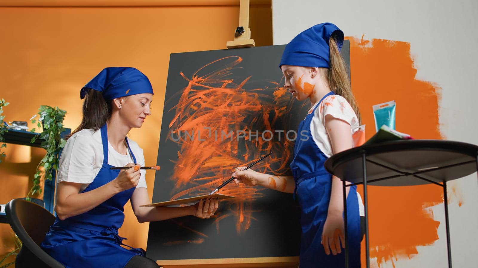 Small family painting artwork design with aquarelle on canvas, holding paintbrush with orange color to create masterpiece. Learning to create artistic model inspiration with dye. Tripod shot.