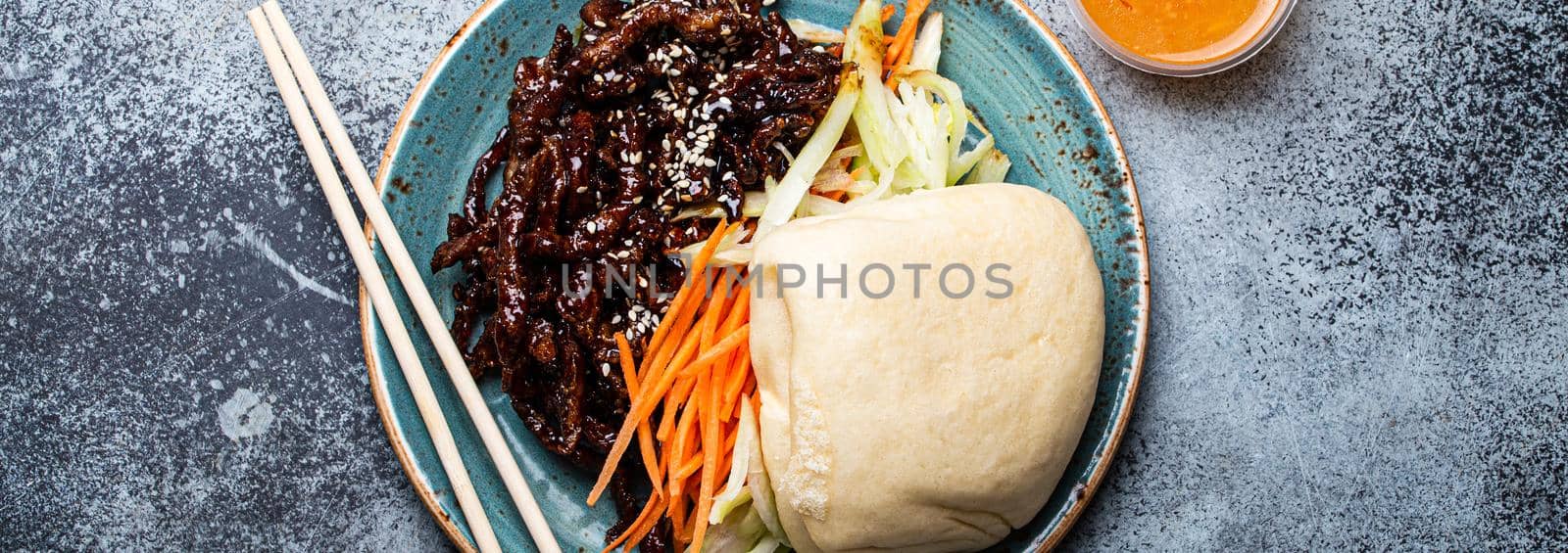 Chinese traditional dish sweet and sour deep fried glazed pork with vegetables and steamed bao bun on plate with on rustic concrete background top view, Asian meal with chopsticks