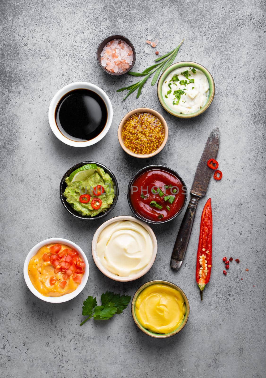 Cooking healthy sauces and dressings concept. Different dips in bowls on rustic concrete background, ingredients, herbs, pepper chili and kitchen knife, top view, close-up