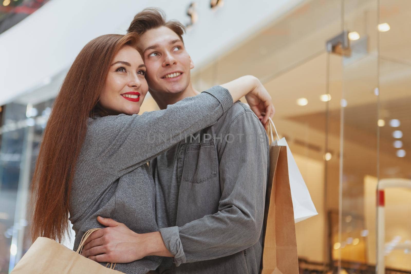 Happy beautiful couple embracing, looking away joyfully while shopping at the mall together. Attractive cheerful woman enjoying shopping spree with her boyfriend, copy space