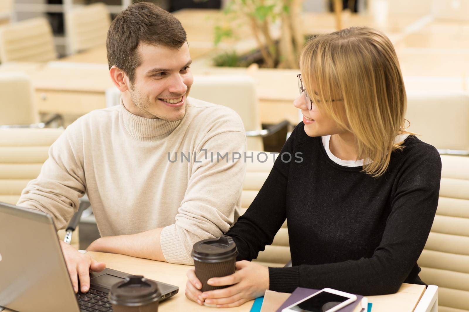 Young businesspeople working together on a laptop. Handsome young man smiling joyfully at his beautiful female colleague sitting at the loft workspace education studying project startup coworkers idea