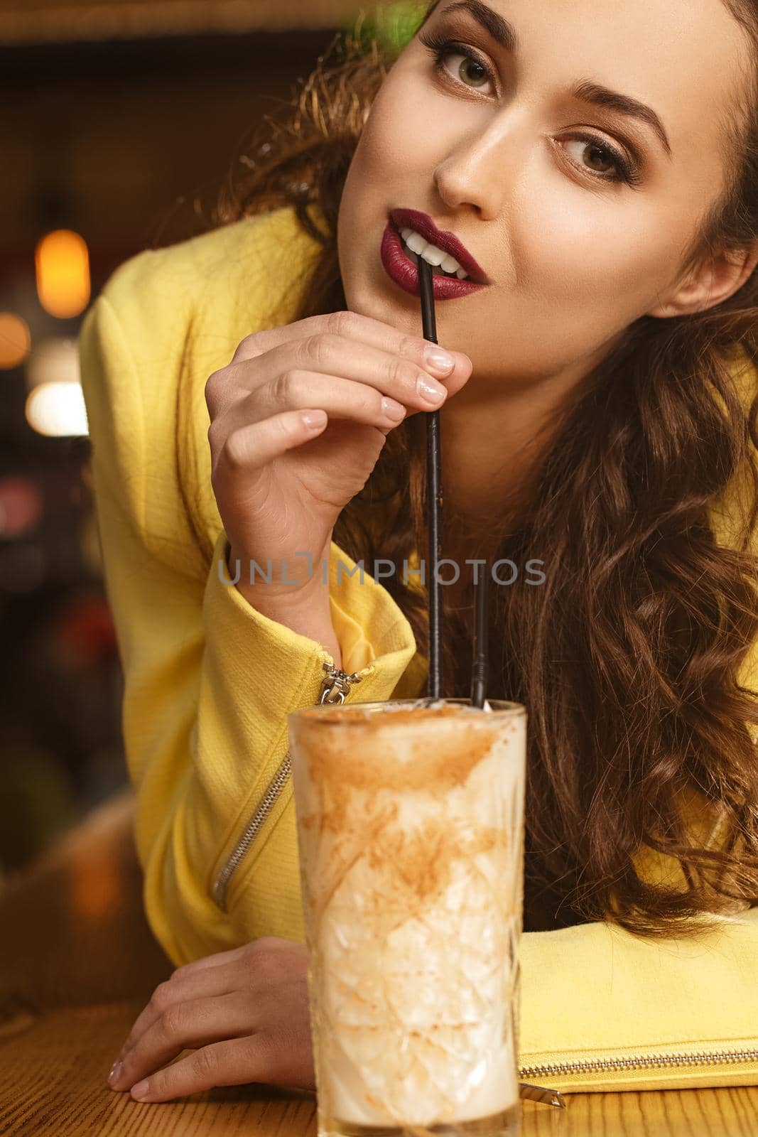 Delightful taste. Vertical portrait of a red lipped brunette sipping her cocktail seductively looking to the camera
