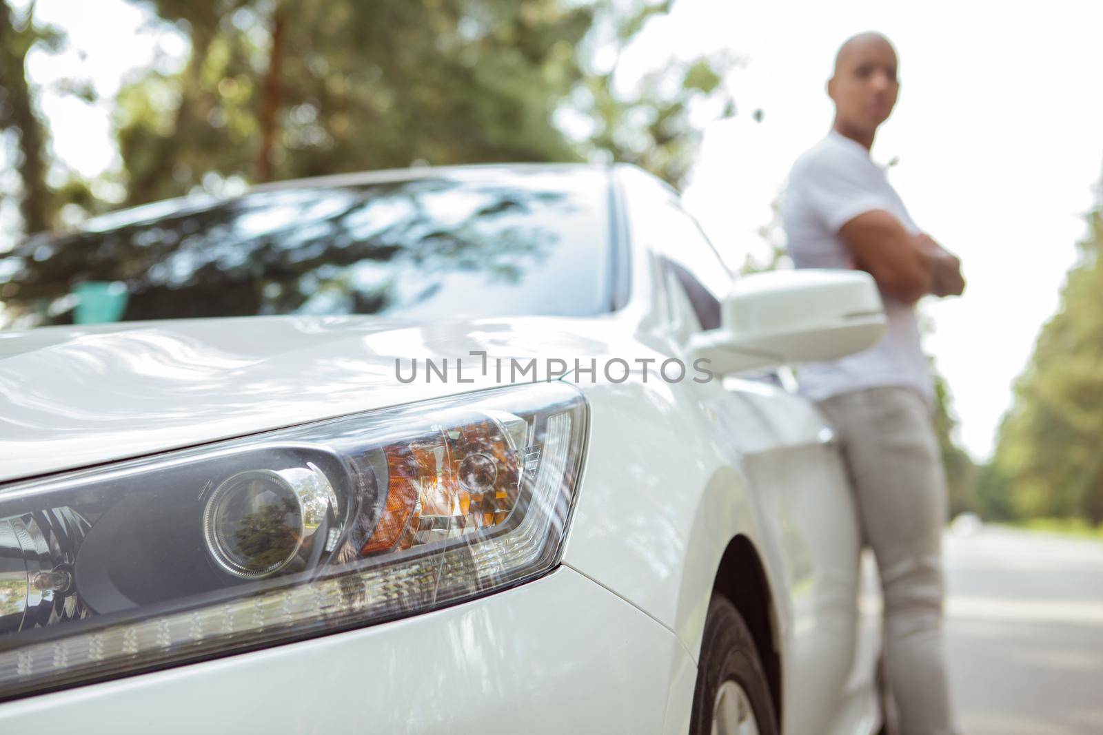 Close up of car lights, male car owner on the background, admiring nature on countryside road. Man travelling by car, taking break from driving on his roadtrip, copy space