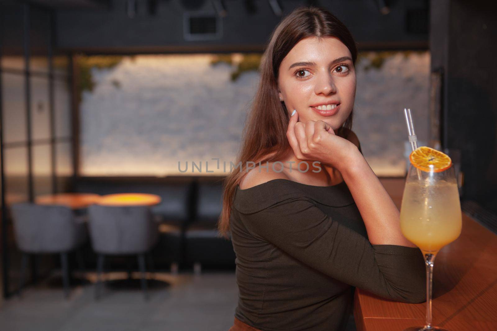 Young beautiful woman relaxing at the bar, having a cocktail, copy space