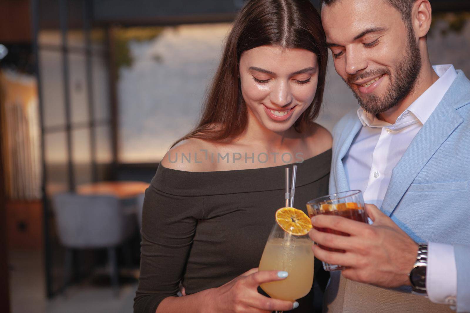 Cropped shot of a young couple cuddling at the bar, while drinking cocktails together, copy space