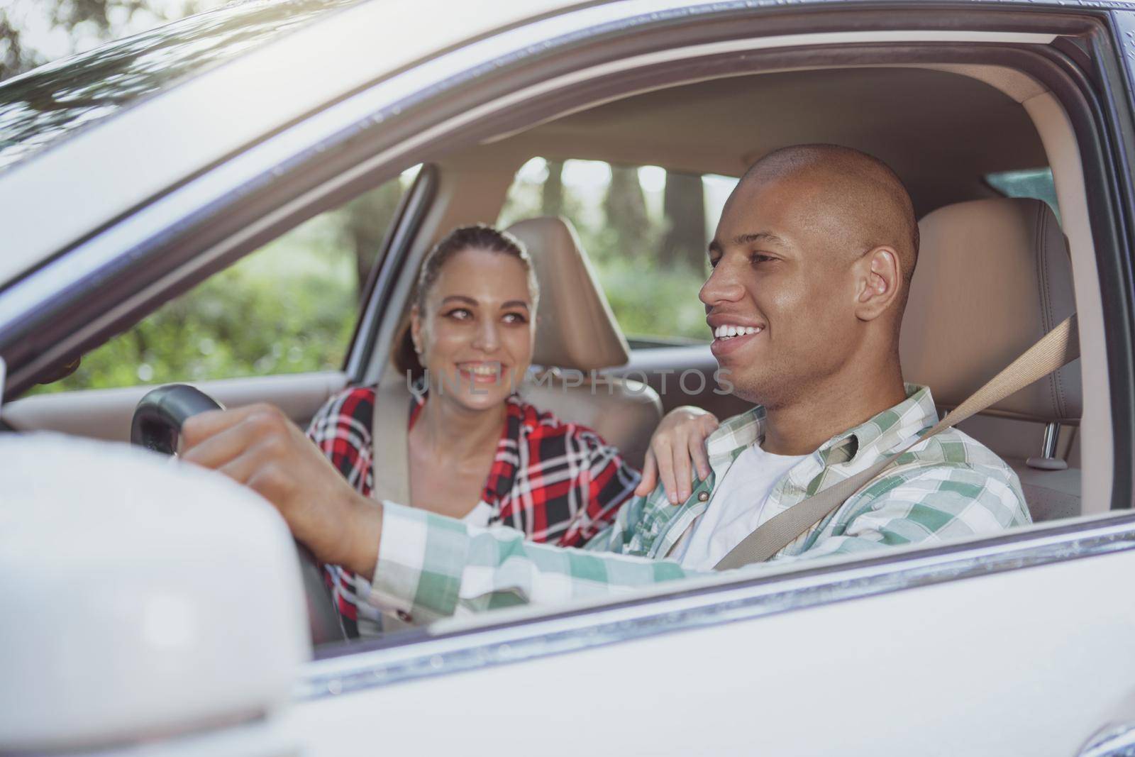 Happy young multiracial couple driving on country road, enjoying travelling together, copy space. Handsome African man smiling, enjoying roadtrip by car with his beautiful girlfriend