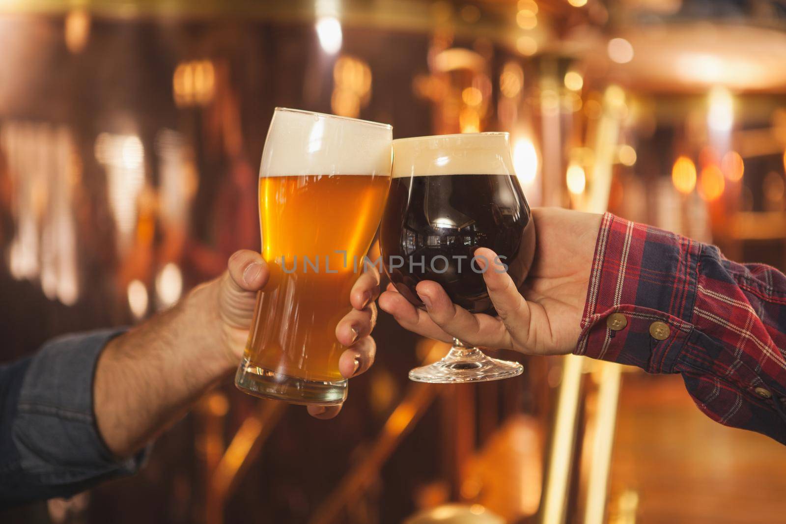 Cropped close up of two men clinking beer glasses together, celebrating at the beer pub. Professional brewers toasting with their beer glasses. Success celebration, oktoberfest festival concept