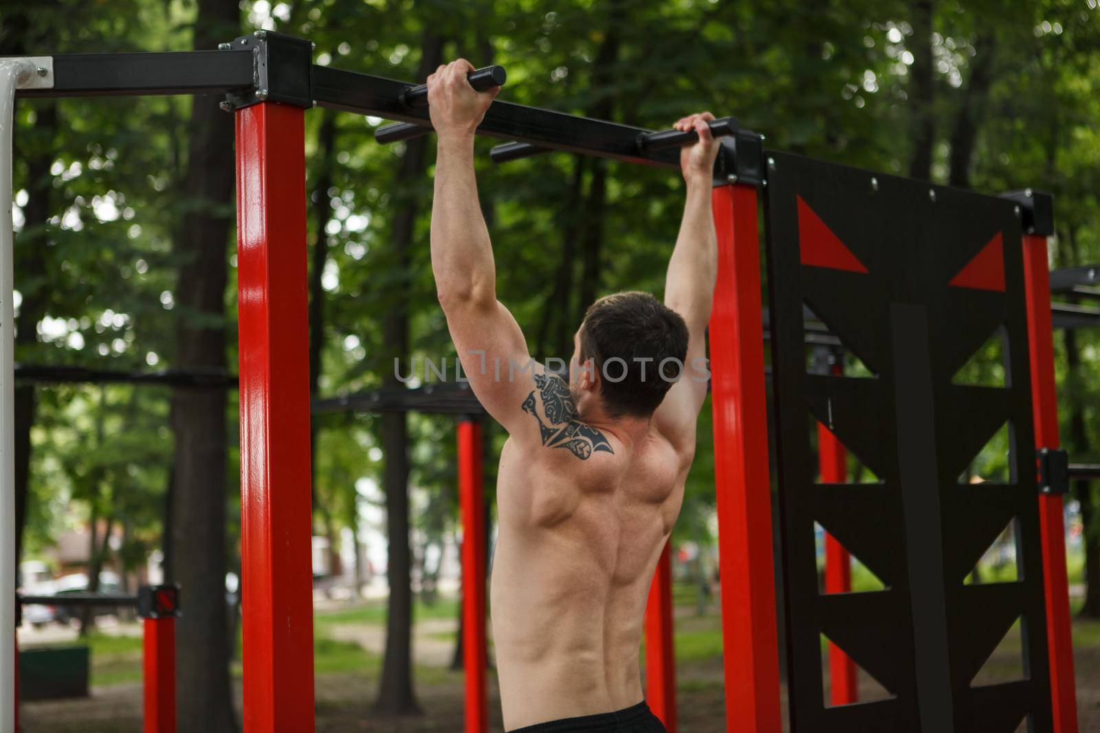Rear view shot of a ripped muscular man doing pull ups outdoors