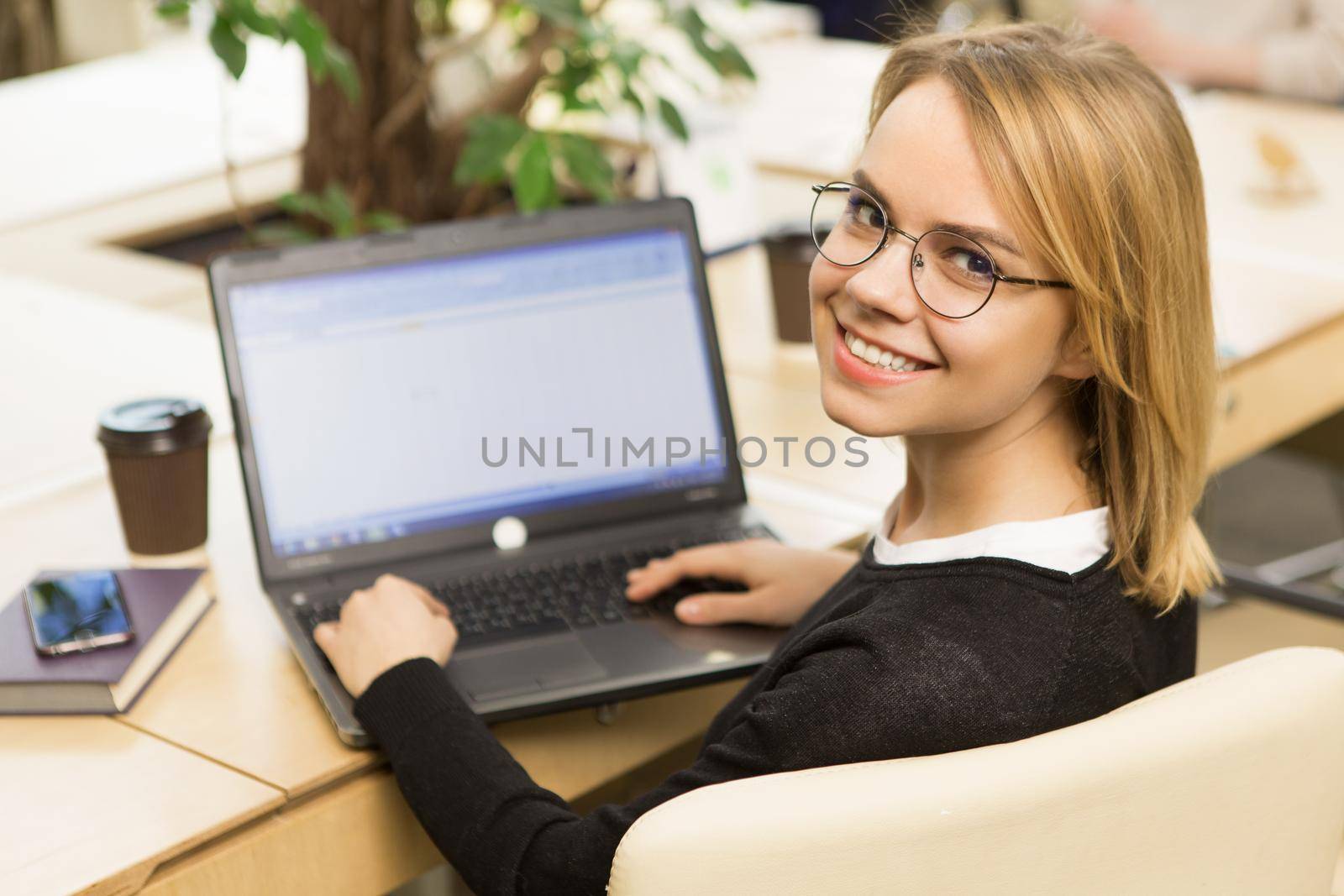 Happy young woman smiling to the camera over her shoulder working on the laptop confidence businesswoman smart casual success startup student studying technology online e-learning internet connect