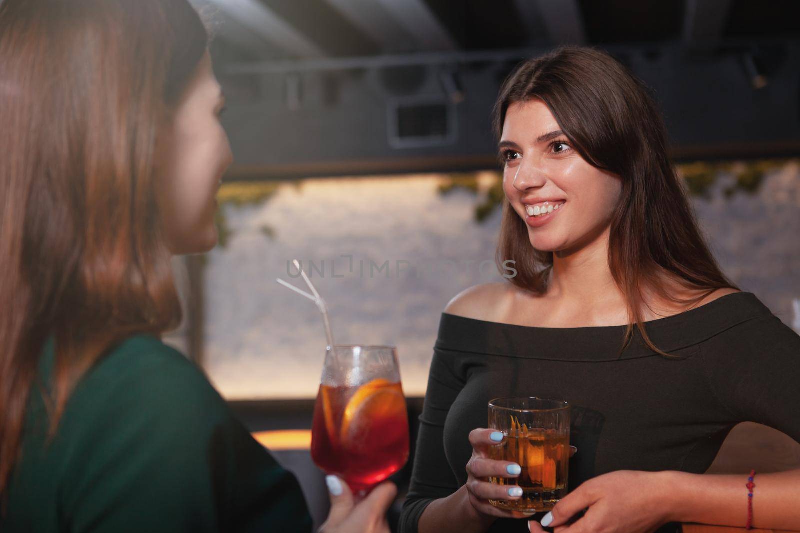 Attractive cheerful woman enjoying drinks with her friend at the restaurant in the evening