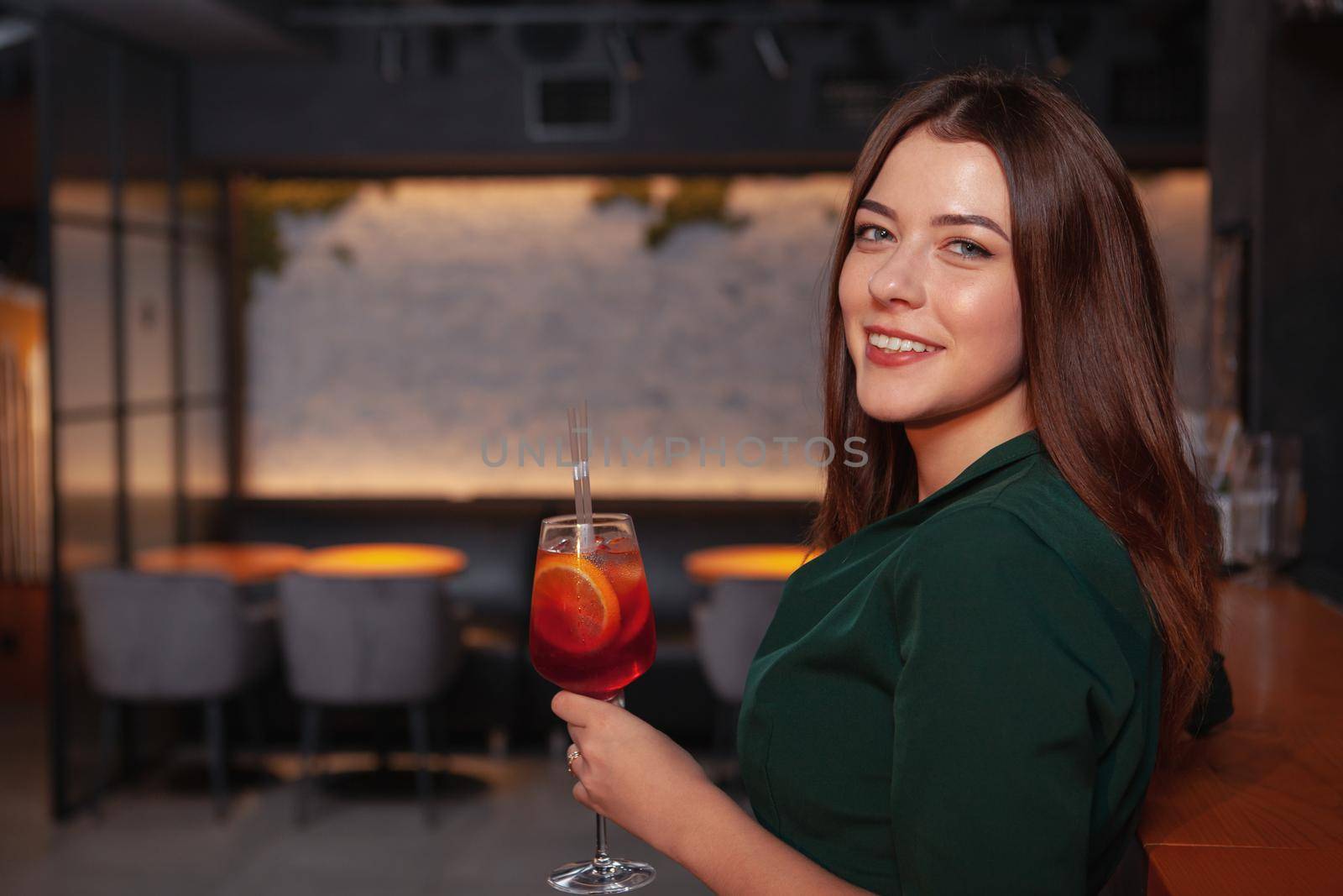 Happy beautiful young woman smiling to the camera while having a drink at the bar