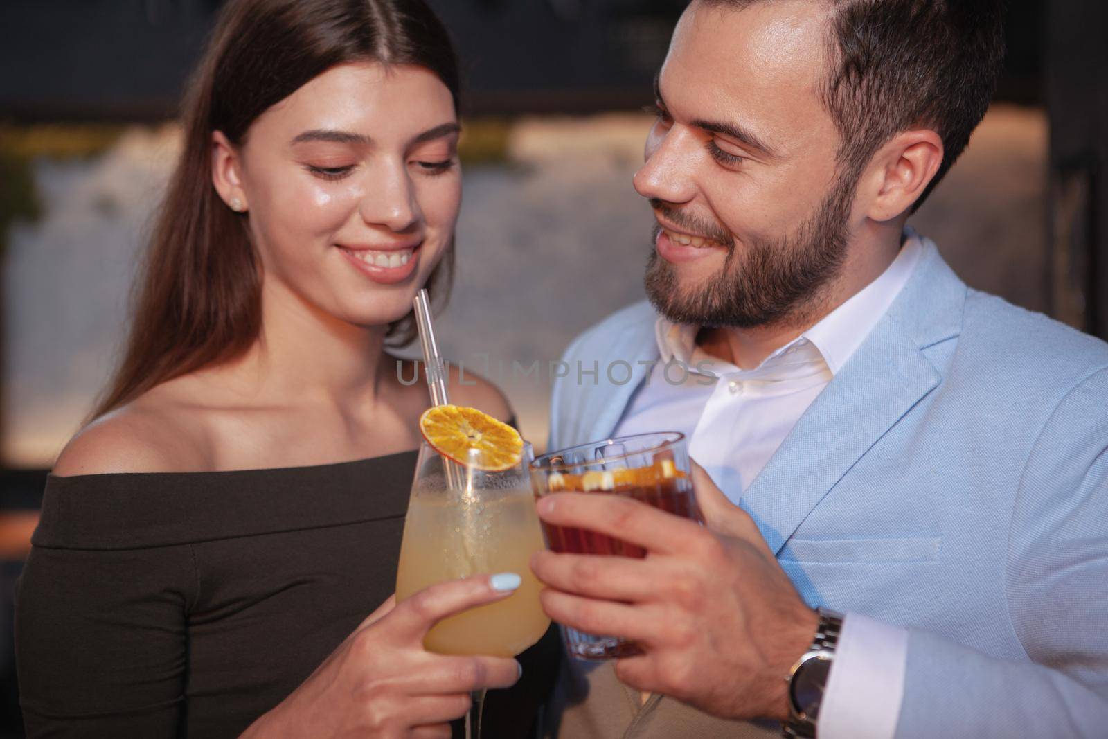 Cropped close up of happy young couple clinking cocktail glasses, enjoying drinks at the bar. Celebration, love, valentines day concept