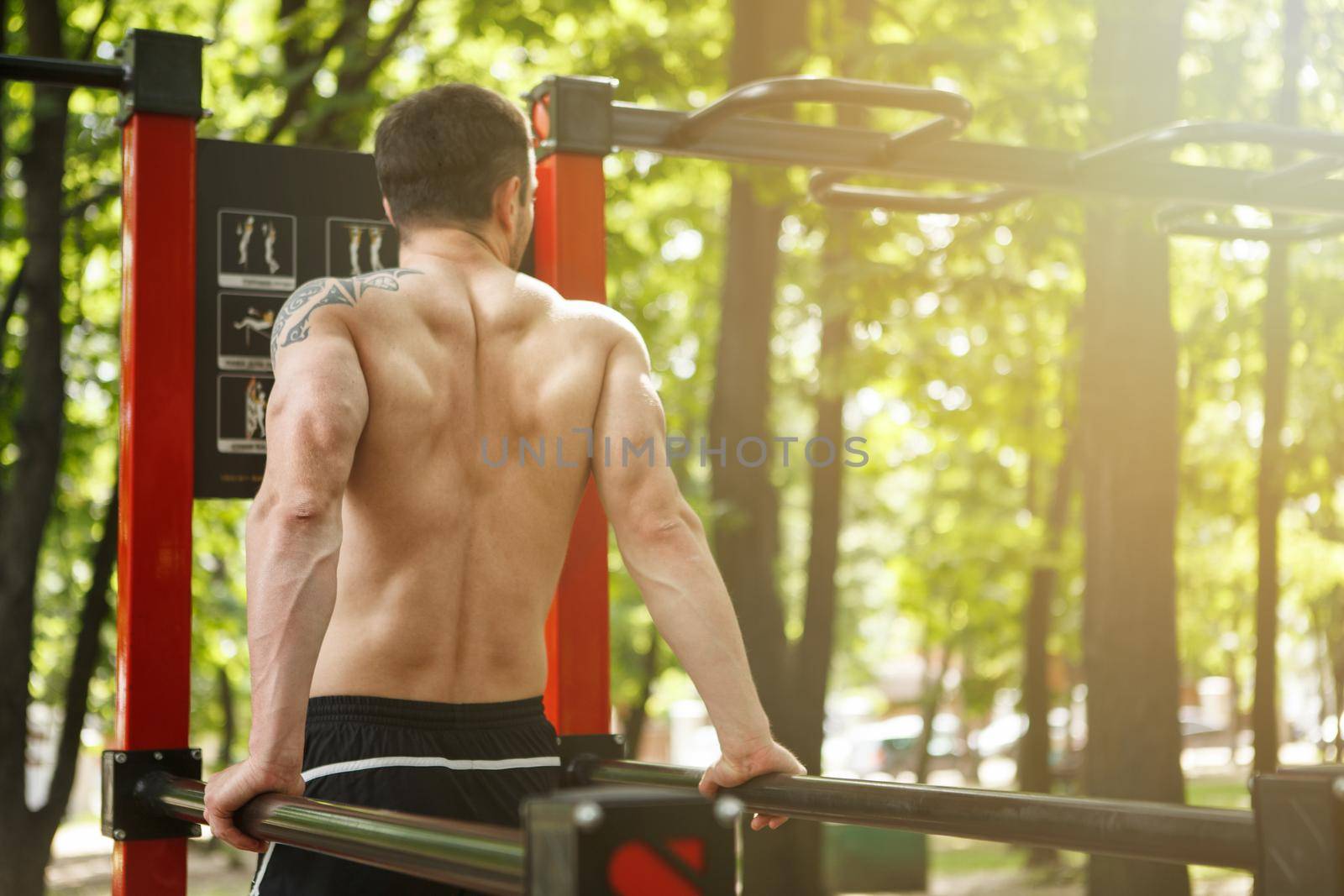 Unrecognizable sportsman working out on calisthenics equipment in the forest
