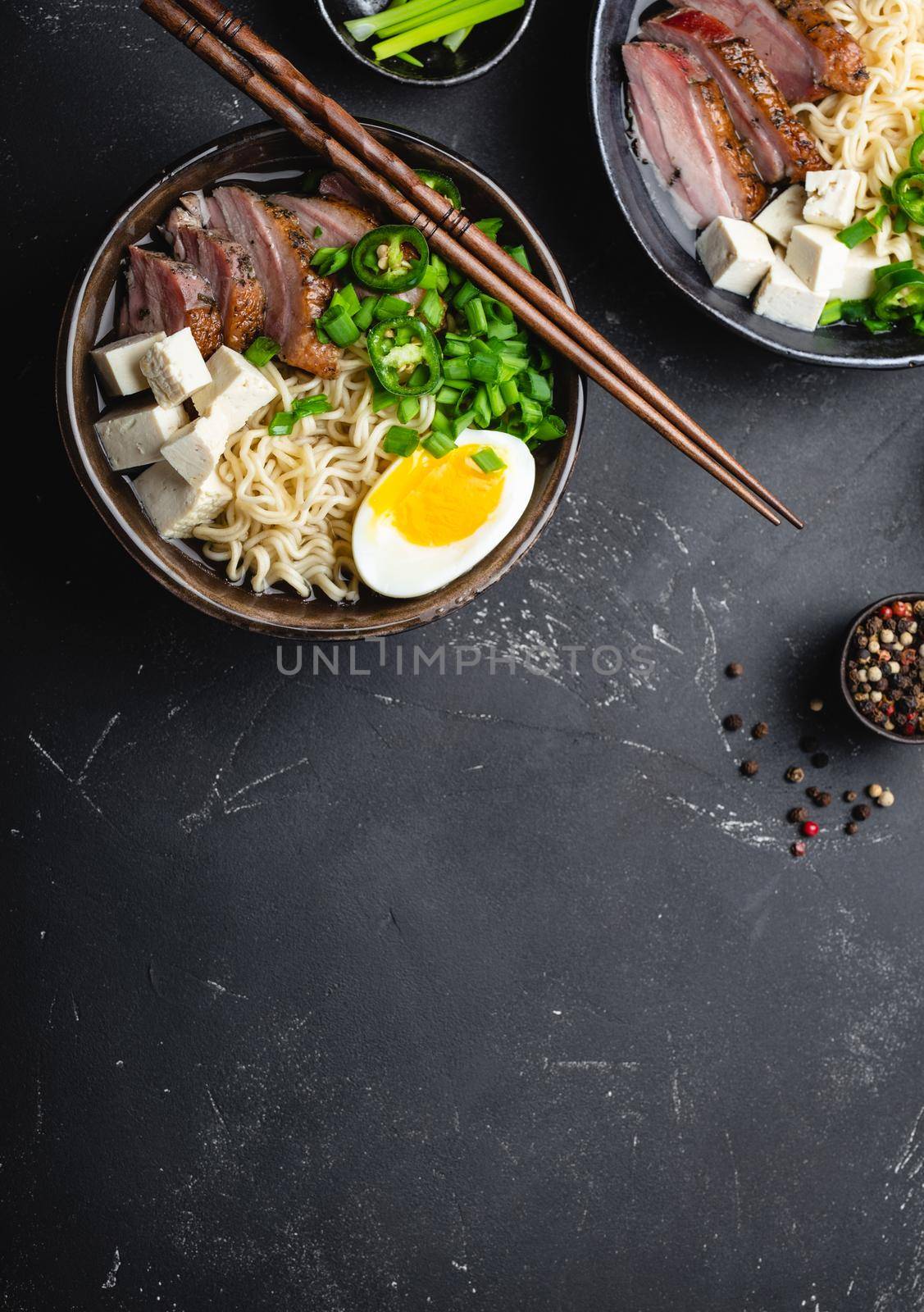 Two bowls of tasty Asian noodle soup ramen with broth, tofu, pork, egg on black rustic stone background, space for text, close up, top view. Hot tasty Japanese ramen soup for dinner with copy space