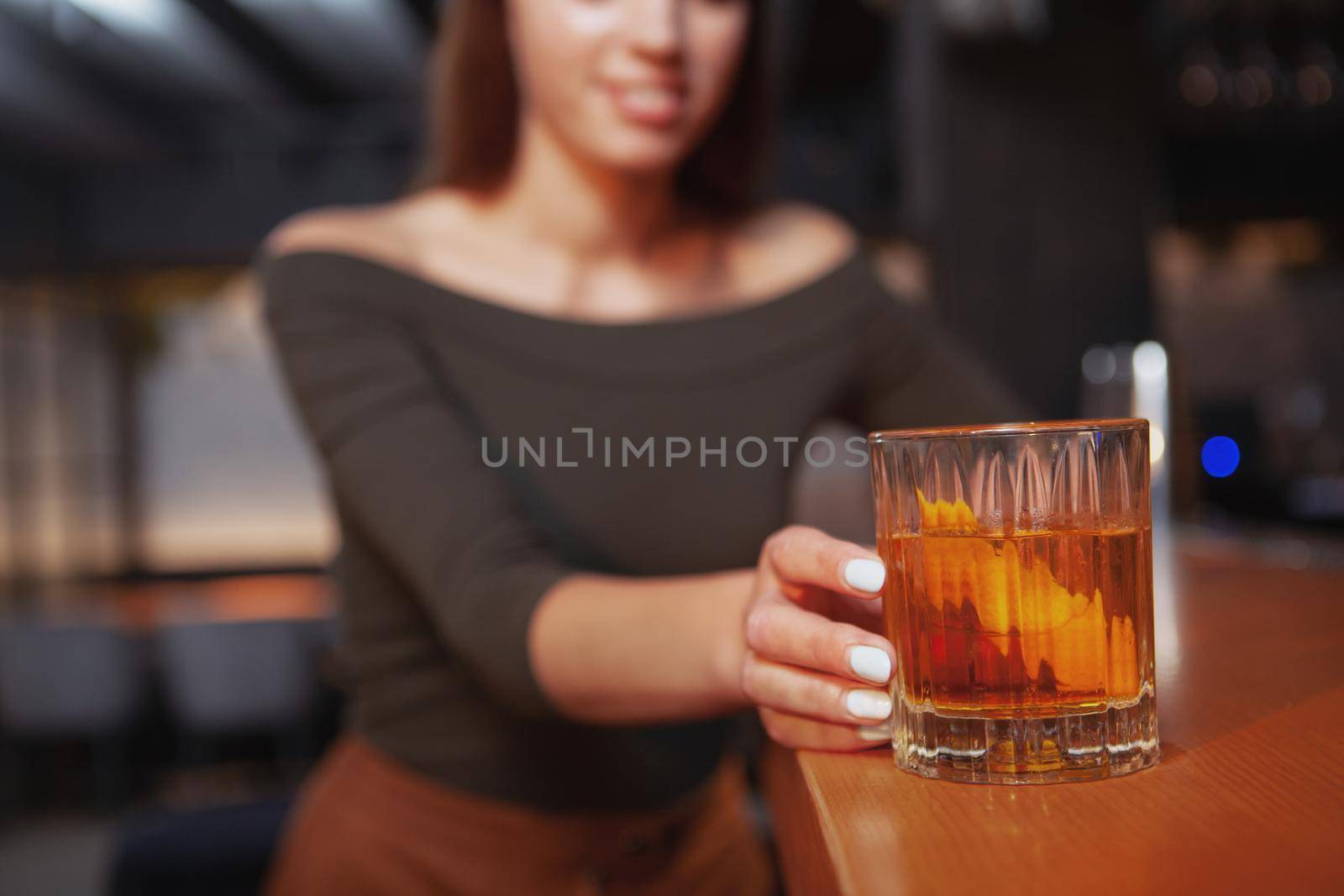 Selective focus on cocktail glass in the hand of a woman at the bar. Female customer at the nightclub having a drink