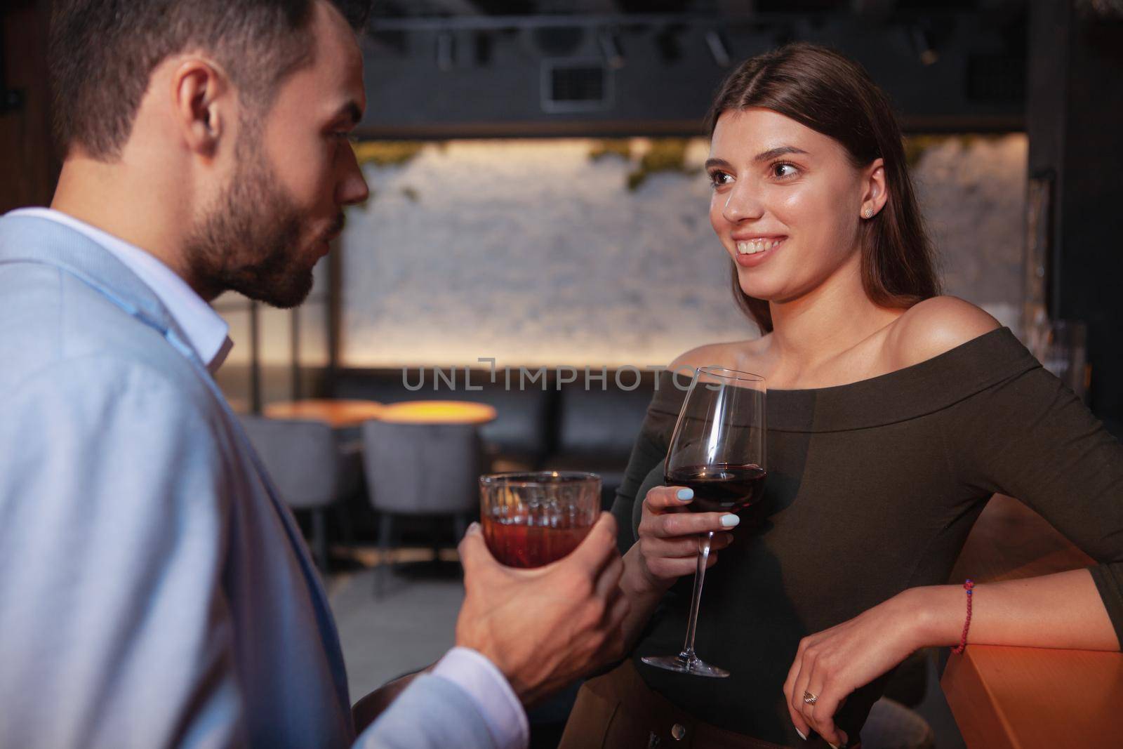Charming happy young woman drinking cocktails with her boyfriend at the bar. Couple enjoying evening at nightclub