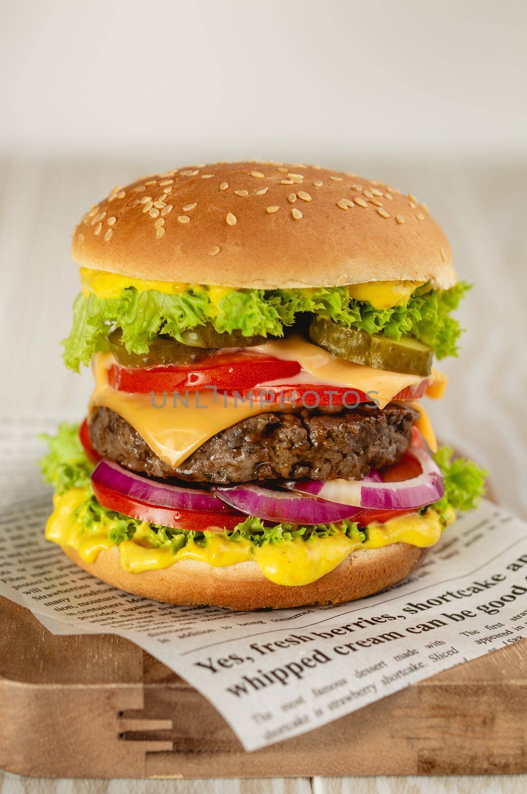 Delicious burger with meat, melted cheese, dripping sauce and vegetables on white rustic background. Freshly made tasty hamburger, close-up.