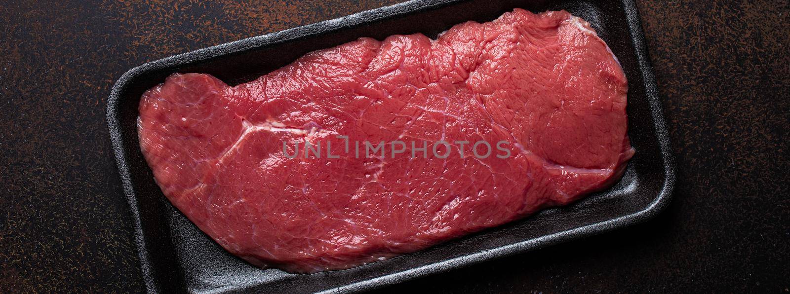 Beef lean raw fillet steak in black plastic container on dark brown rustic concrete background from above flat lay, diet beef meat steak ready to be cooked