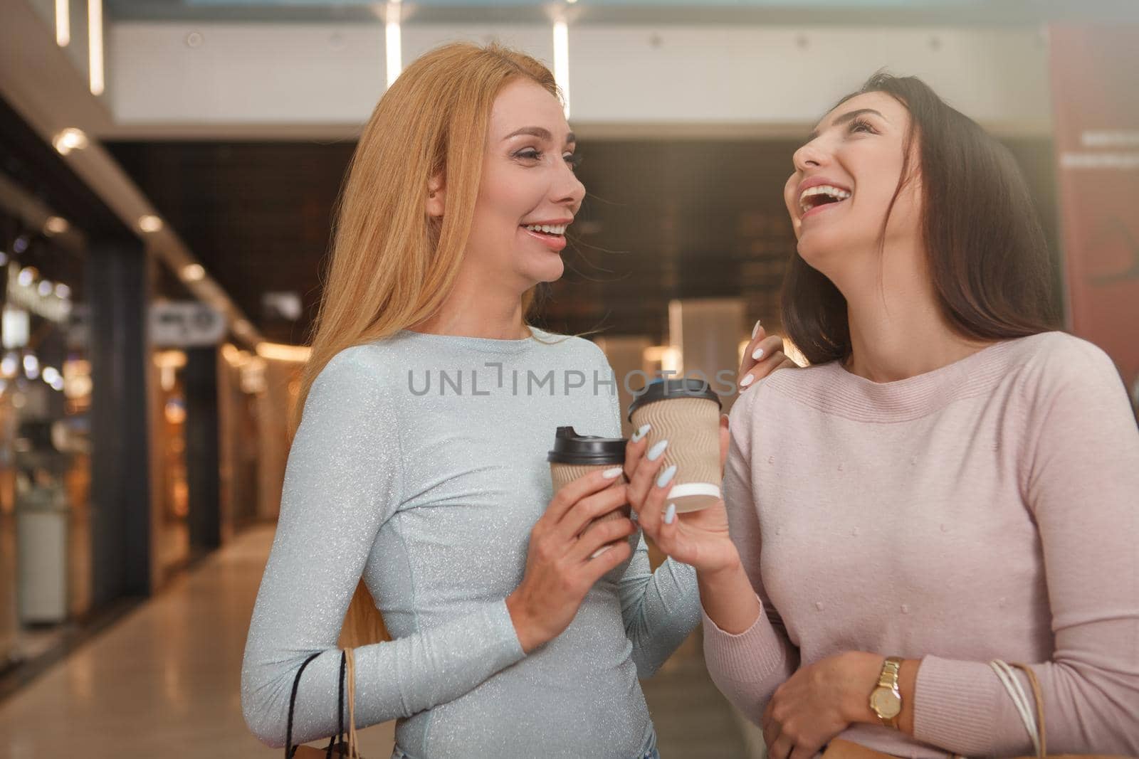 Happy beautiful female friends laughing, enjoying coffee while shopping together at the mall
