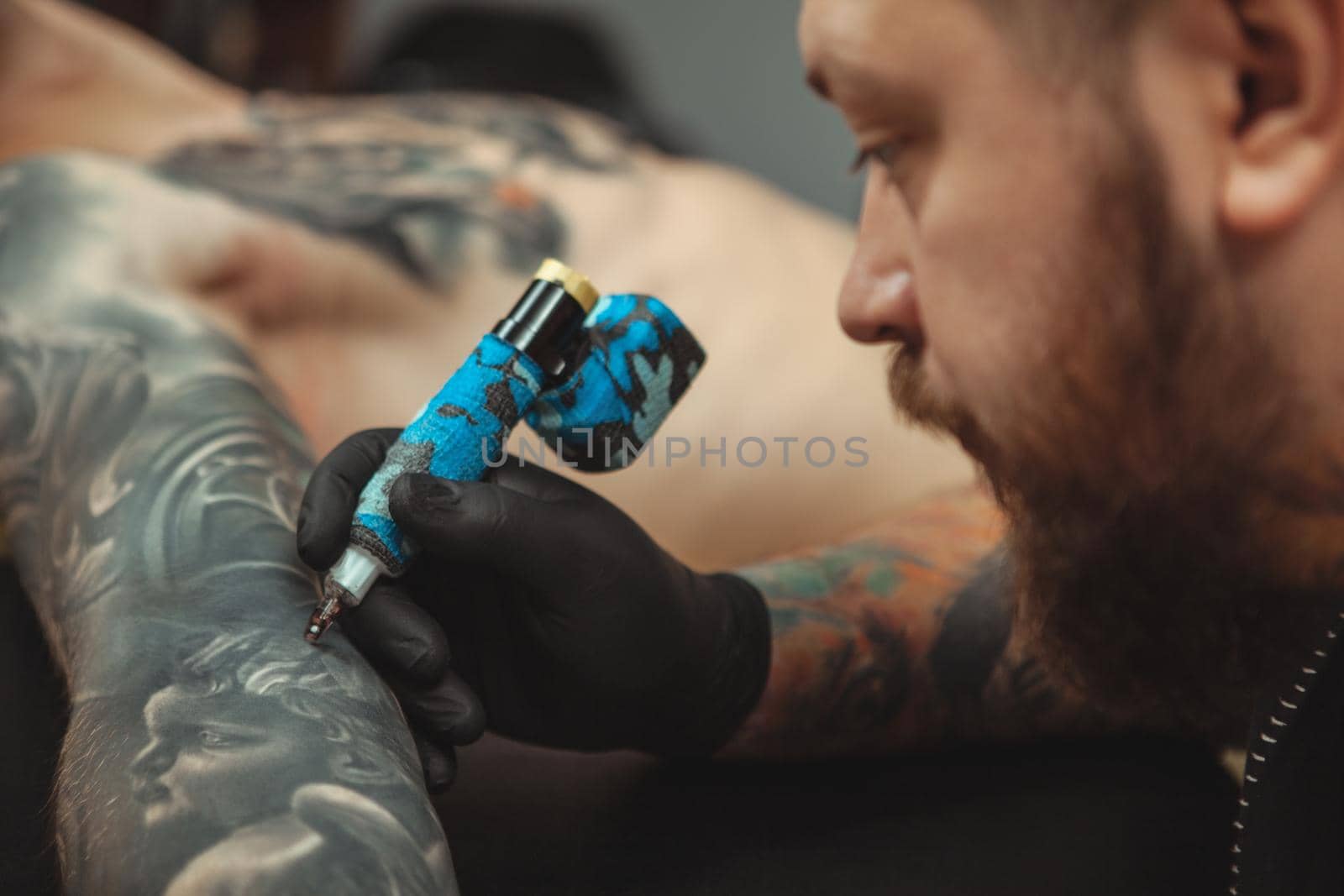 Bearded tattooist making tattoos on body of his client by MAD_Production
