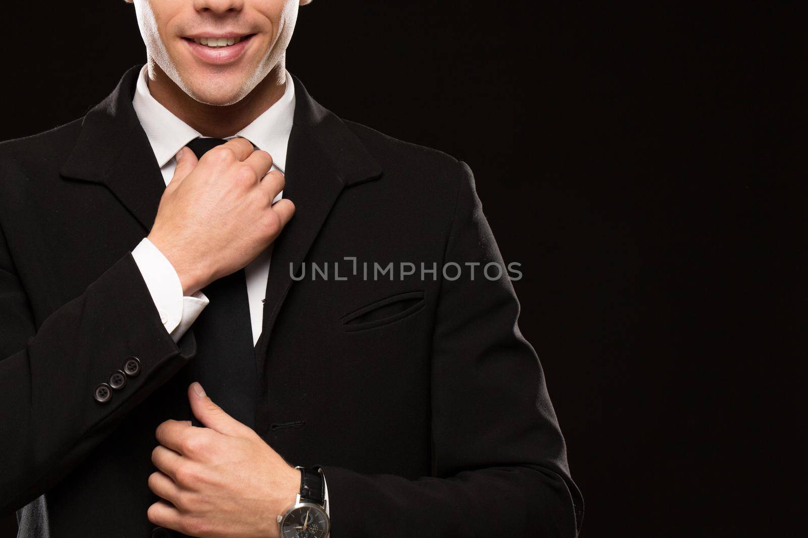 Cropped shot of a handsome man wearing elegant black suit smiling adjusting his tie on black background copyspace positivity confidence businesspeople success preparing preparation wellbeing
