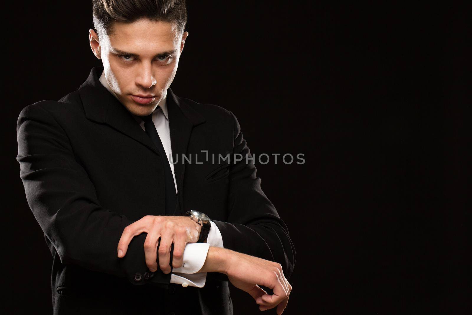 Profesional bodyguard wearing black suit and tie rolling up his sleeves aggressively preparing to fight on black background copyspace protection safety profession brutality masculinity conflict