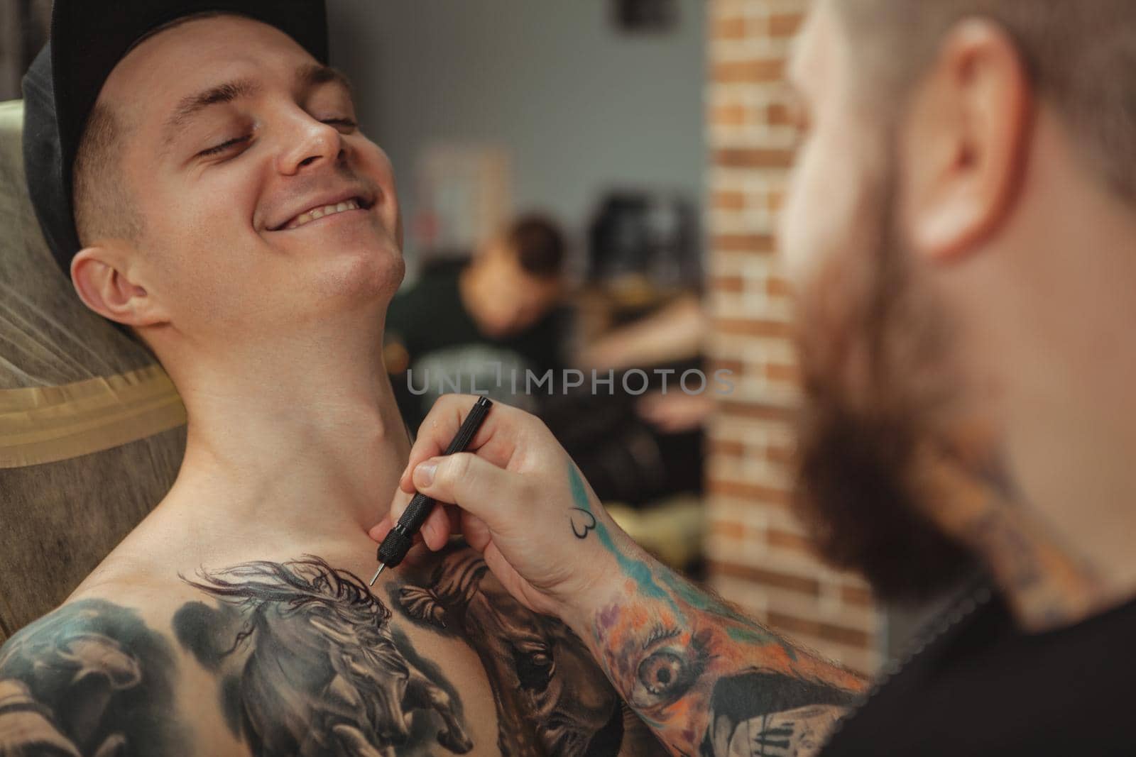 Cropped shot of a cheerful handsome man smiling, preparing to get a new tattoo. Rear view shot of a professional tattoo artist sketching on the body of his client before tattooing. Alternative art concept