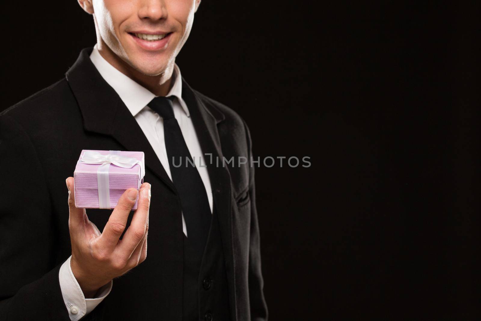 Cropped shot of an attractive suited man holding out a gift with a bow to the camera smiling seductively on black background copyspace love romance relationships dating valentines surprise