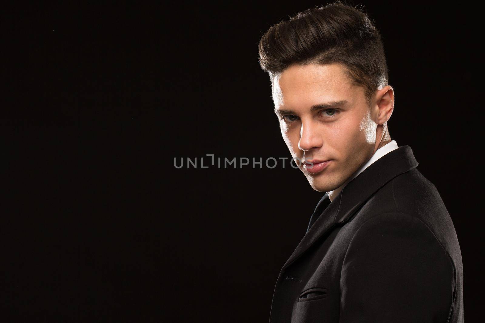 Close up portrait of a handsome professional secret service agent looking to the camera over his shoulder on black background suit professionalism confidence serious masculine guar bodyguart protection